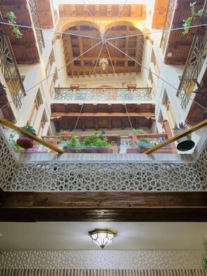 A multi-level atrium with wooden beams, a patterned floor, and hanging plants. - SAFIYA BOUTIQUE HOTEL (Buxoro)