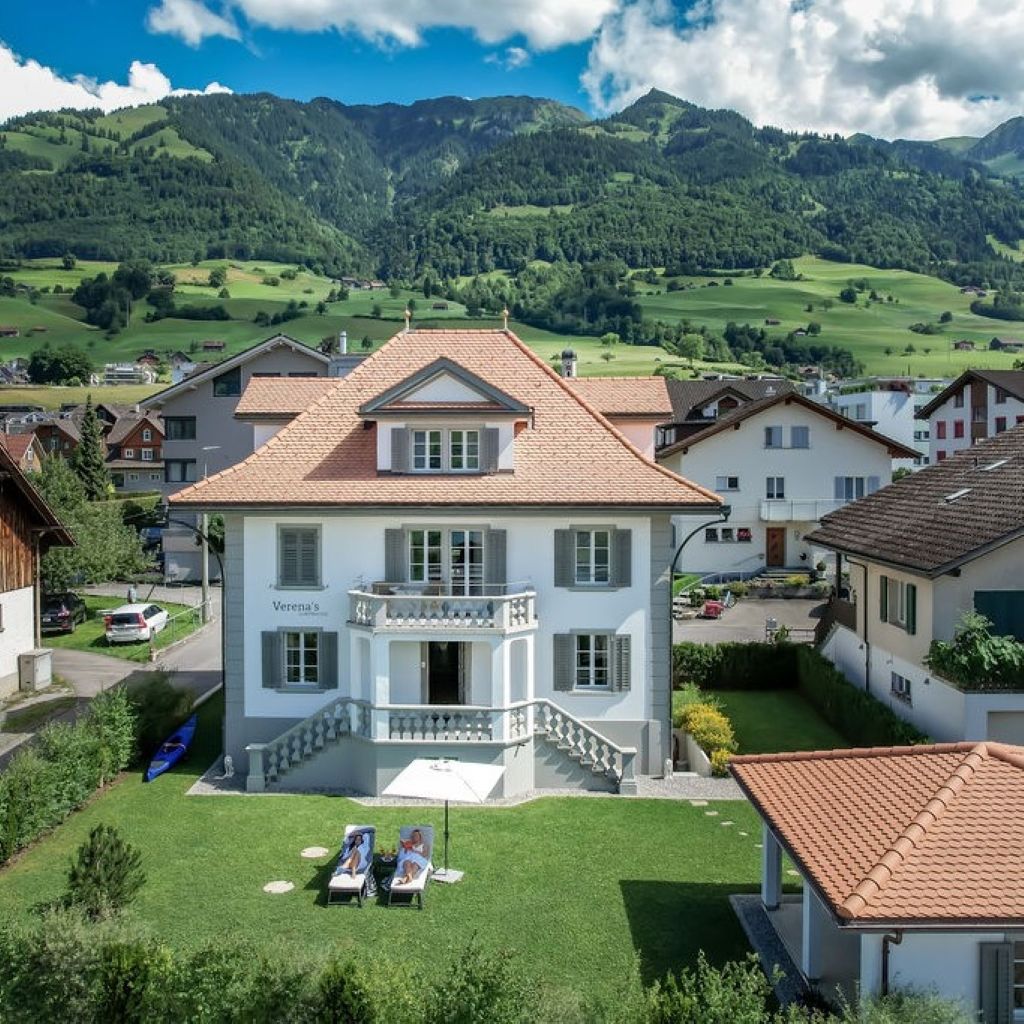 Ein zweistöckiges Haus mit Balkon, umgeben von einem gepflegten Rasen und einer Bergkulisse.