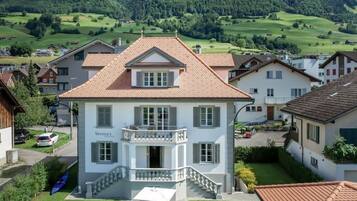 Ein zweistöckiges Haus mit Balkon, umgeben von einem gepflegten Rasen und einer Bergkulisse.