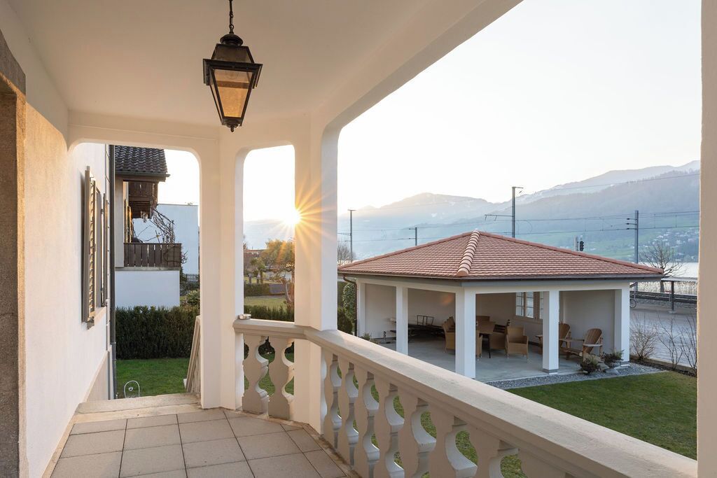 A balcony with a view of a lake and mountains, a covered patio area, and a hanging lantern.
