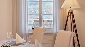 A dining area with a table set for two, a lamp, and a view through a window.