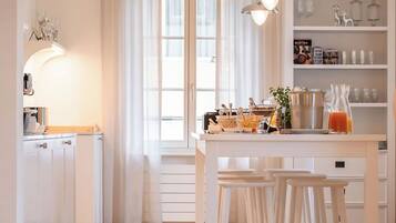 Une cuisine moderne avec des meubles blancs, un coin repas doté de tabourets et une grande fenêtre agrémentée de rideaux.