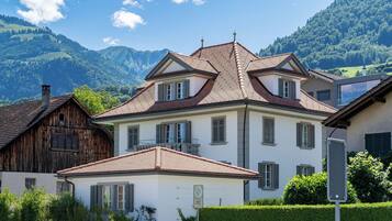 Une maison à deux étages, dotée d’un toit en pente, d’un balcon et offrant une vue sur une chaîne de montagnes.