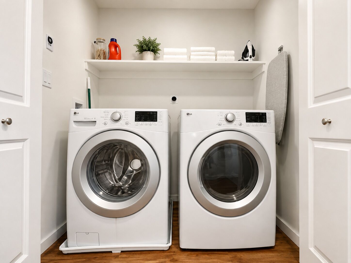 A laundry room with two white LG front-loading washing machines, a shelf above with cleaning supplies, and a towel rack.