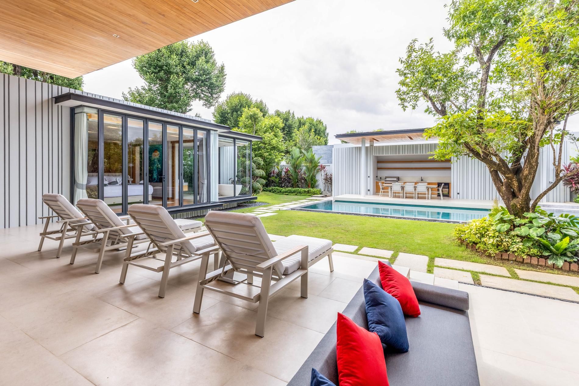 Un espacio exterior moderno con piscina, sillas de descanso y una estructura con paredes de vidrio.