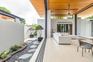 A modern outdoor living space with a white sofa, a dining table, and potted plants. - Botanica Forestique 4br Luxury Retreat (Choeng Thale)