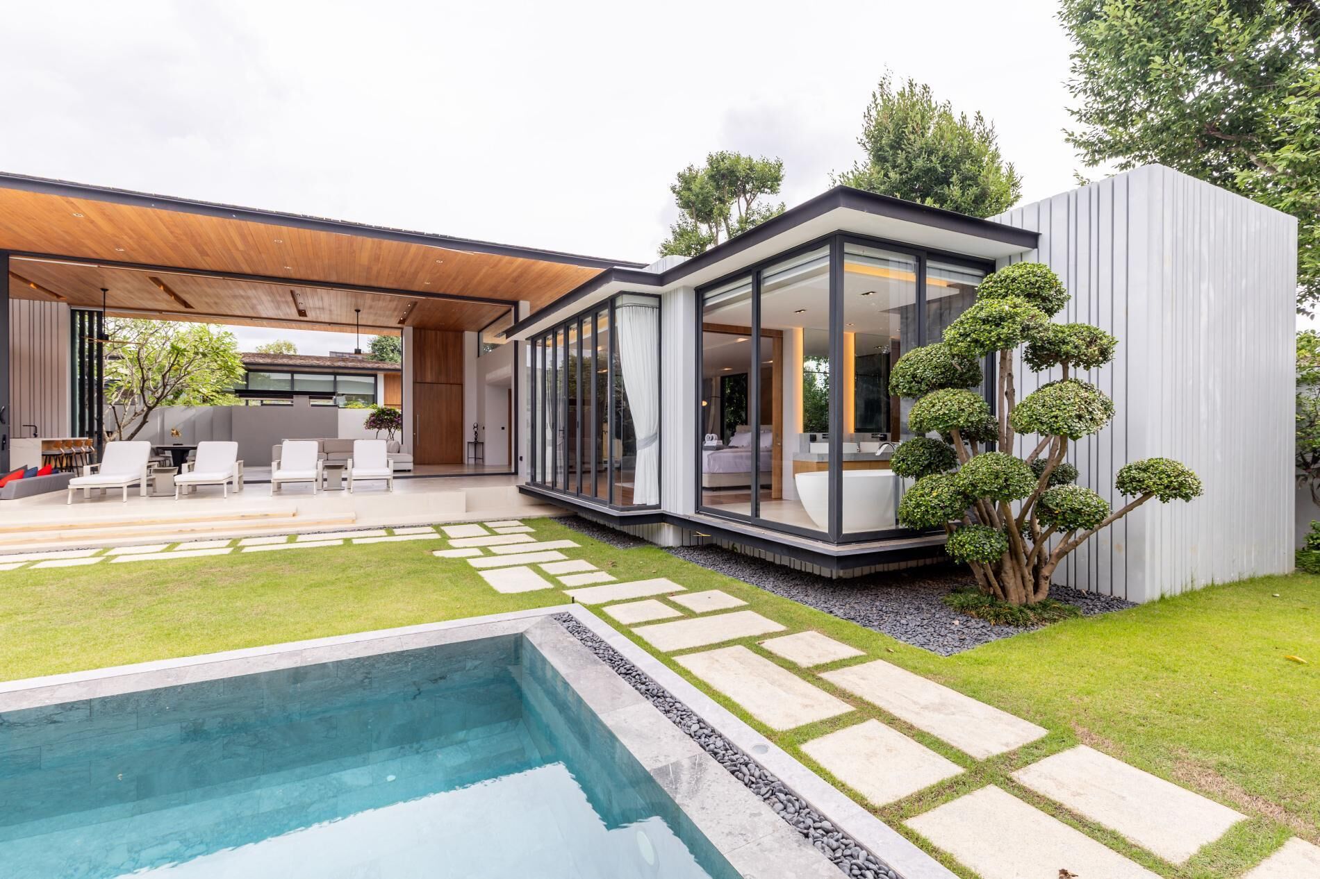 Una casa moderna con piscina, mobiliario exterior y un jardín cuidado.
