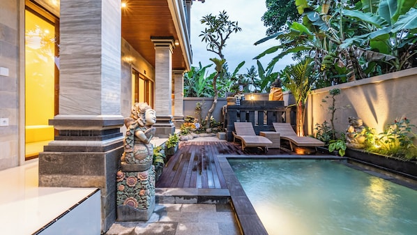 A pool area with a wooden deck, lounge chairs, and a statue. - Lavana Ubud (Ubud)