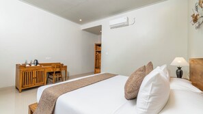 Een hotelkamer met een bed, nachtkastje, lamp, houten garderobe en een bureau met stoel.