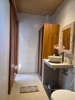 Een badkamer met een houten deur, een beige wastafel met een kom, een spiegel en een handdoek op de vloer.