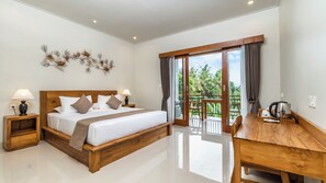A hotel room with a wooden bed, a dining table, and a balcony with a view of greenery. - Lavana Ubud (Ubud)
