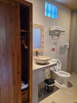 Un baño con puerta de madera, un lavamanos redondo, un inodoro, un perchero para toallas y una ventana pequeña.
