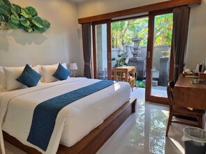A hotel room with a large bed, a desk, and a view of the garden through the sliding doors. - Lavana Ubud (Ubud)