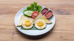 Een bord met gebakken eieren, toast, komkommer, tomaat, sla en twee sauzen.