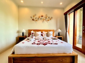 A neatly made bed with a heart-shaped arrangement of rose petals, two swan-shaped pillows, and a decorative wall piece above it. - Lavana Ubud (Ubud)