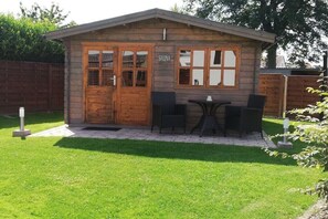 Eine Holzhütte mit Sauna, einer kleinen Terrasse mit Tisch und Stühlen sowie einem gepflegten Rasen.