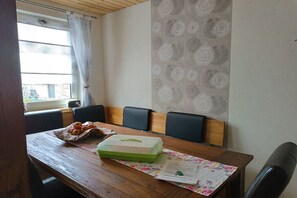 A dining area with a wooden table, a green container, and a floral tablecloth. - Holiday apartment Wolkenbruch (Trendelburg \/Friedrichsfeld)