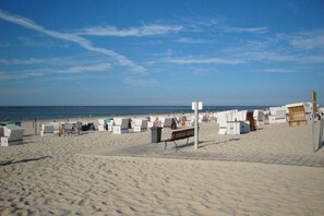 A beach with rows of white beach chairs and umbrellas, a wooden bench, and a clear blue sky. - Holiday apartment with 2 bedrooms (Baltrum)