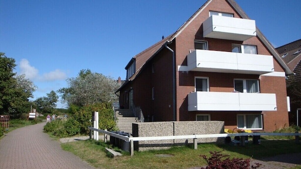 A two-story residential building with a brick facade, a stone pathway leading to the entrance, and a gated driveway. - Holiday apartment with 2 bedrooms (Baltrum)