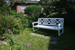 A white bench in a garden with a brick building in the background. - Holiday apartment with 2 bedrooms (Baltrum)