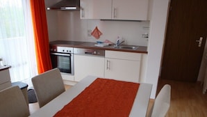 A compact kitchen with a stove, oven, and sink. There is a dining table with chairs and a red patterned table runner. - Holiday apartment with 2 bedrooms (Baltrum)