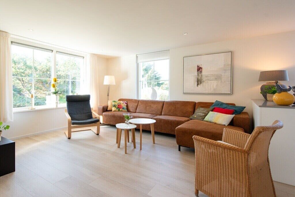 Un salon moderne avec un canapé, un fauteuil et une table basse, de grandes fenêtres et un tableau accroché au mur.