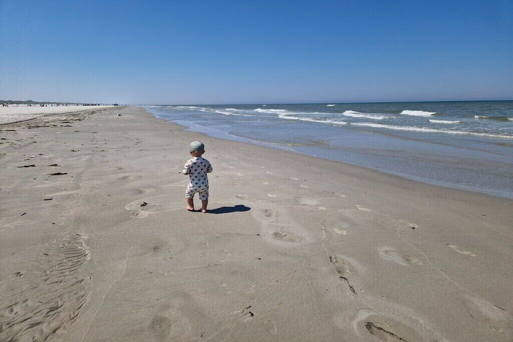 A child standing on a sandy beach with footprints leading to the water.