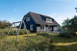 A two-story house with a dark blue exterior, a sloped roof, and a swing set in the front yard. - Holiday apartment in Buren with swimming pool (Buren)
