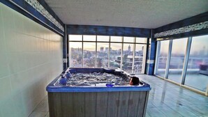 Un jacuzzi en una habitación con amplios ventanales con vistas a un paisaje urbano.