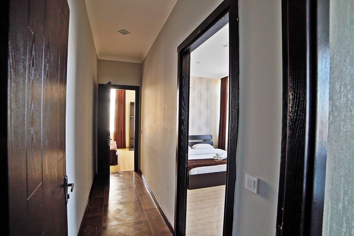 A hallway leading to a bedroom with a bed, a door, and a light switch.