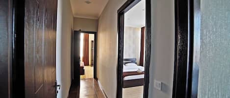 A hallway leading to a bedroom with a bed, a door, and a light switch.