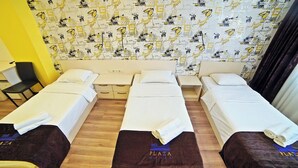 A hotel room with three single beds, a small desk, a chair, and a patterned wall. - Plaza Inn Batumi (Batumi)