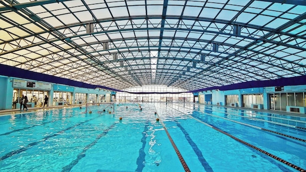 An indoor swimming pool with multiple lanes, a high ceiling with a glass structure, and a blue poolside area. - Plaza Inn Batumi (Batumi)
