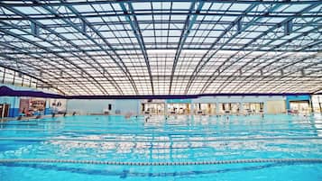 An indoor swimming pool with multiple lanes, a high ceiling with a grid-like structure, and various poolside amenities.