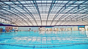 An indoor swimming pool with multiple lanes, a high ceiling with a grid-like structure, and various poolside amenities. - Plaza Inn Batumi (Batumi)