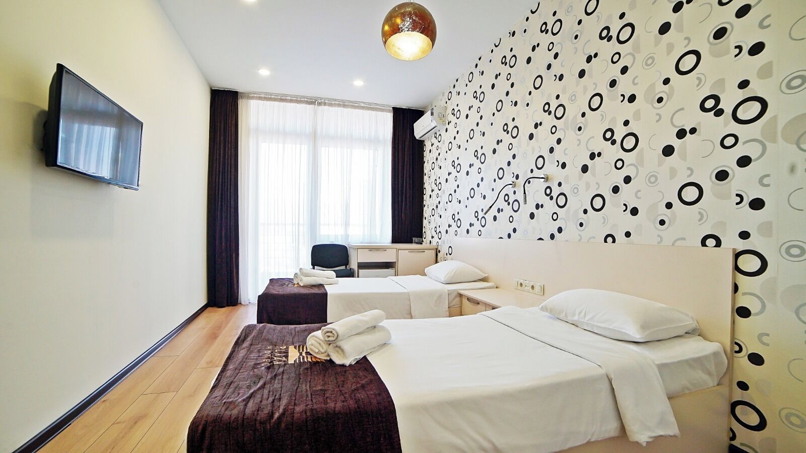 A hotel room with two beds, a desk, a chair, and a TV mounted on the wall.