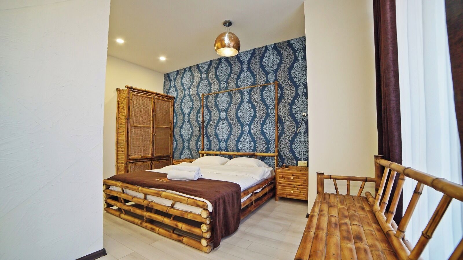 A room with a bed, a wooden chair, a nightstand, and a wall with a patterned wallpaper.