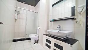 A bathroom with a white toilet, a sink with a black countertop, and a shower area. - Plaza Inn Batumi (Batumi)