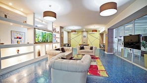 A modern living room with a sofa, armchairs, a coffee table, and a television. There are shelves with decorative items and a large window. - Plaza Inn Batumi (Batumi)