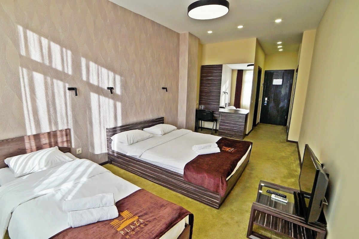 A hotel room with two beds, a desk with a chair, a TV, and a bathroom visible in the background.