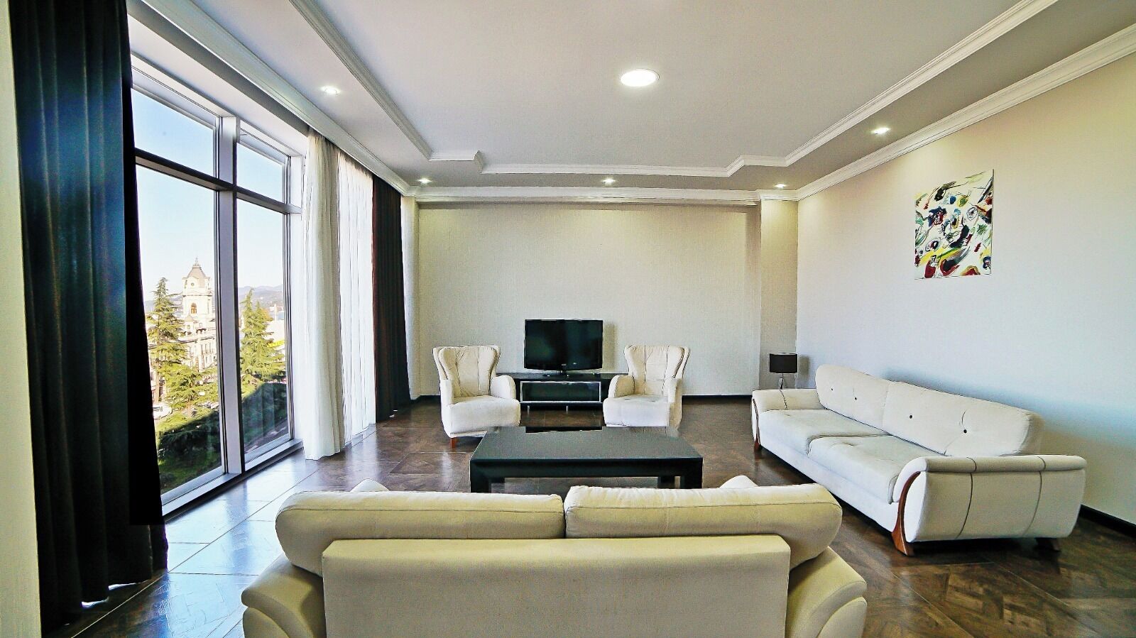 Un salon moderne doté d’une grande fenêtre, d’un téléviseur à écran plat, d’un canapé, de deux fauteuils et d’une table basse.