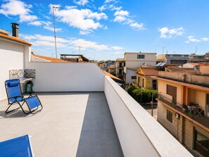 Eine Dachterrasse mit einem Stuhl, einem Tisch und Blick auf umliegende Gebäude.