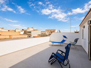 Eine Dachterrasse mit zwei blauen Lounge-Stühlen, einer weißen Wand und freiem Blick auf die Stadtlandschaft.