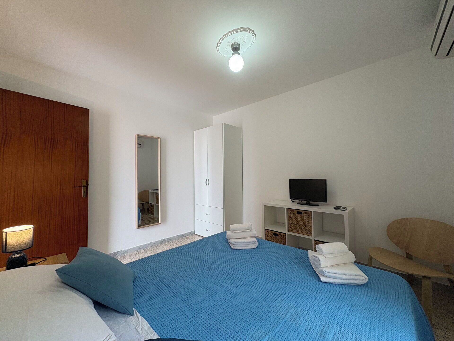 Une chambre à coucher avec un lit, une télévision, une armoire et un miroir.