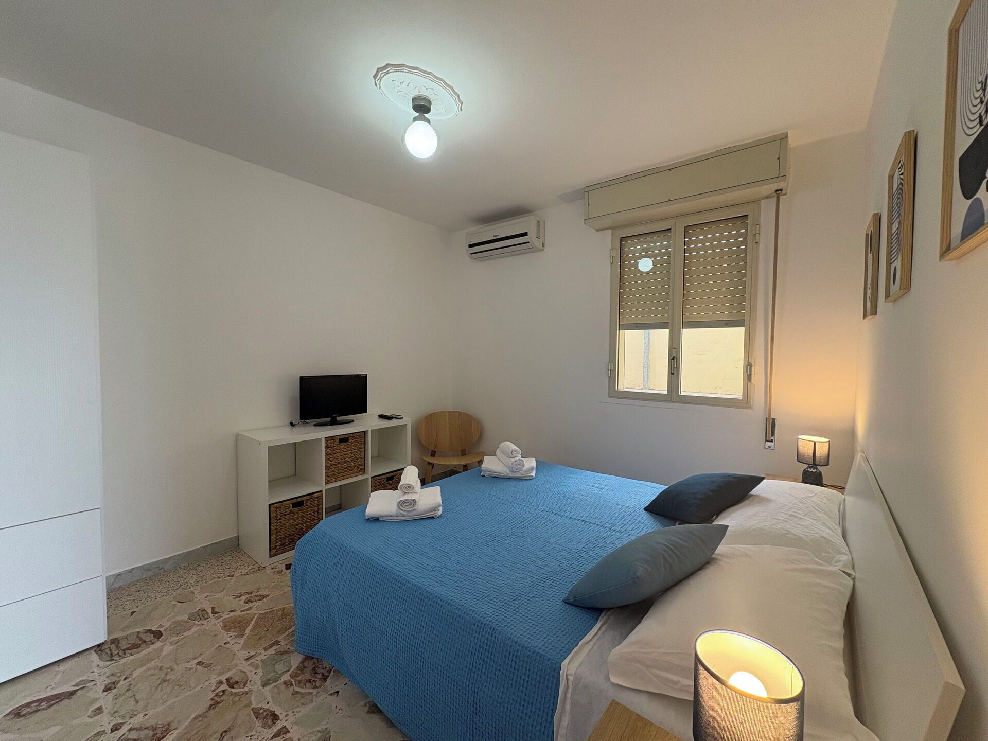Une chambre à coucher comprenant un lit, un téléviseur, une chaise, une fenêtre et un climatiseur fixé au mur.