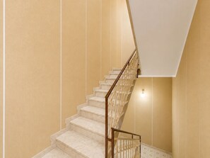 Un escalier avec des marches en marbre et une rampe en bois, menant à un palier où se trouve un luminaire.
