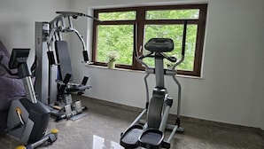 Un gimnasio en casa con equipo de ejercicio, una ventana con vista a follaje y una silla morada.
