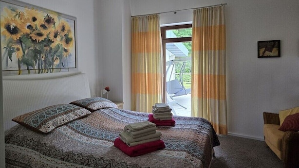 Un dormitorio con una cama, un cuadro de girasoles, una ventana con cortinas y vistas al exterior.