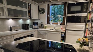 Una cocina moderna con estufa integrada, cafetera y ventana con vista a árboles.