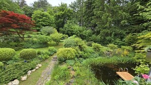 Un jardín exuberante con un estanque, un sendero de piedra y un muelle de madera.
